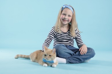 Photo of Little girl with her cute ginger cat on light blue background