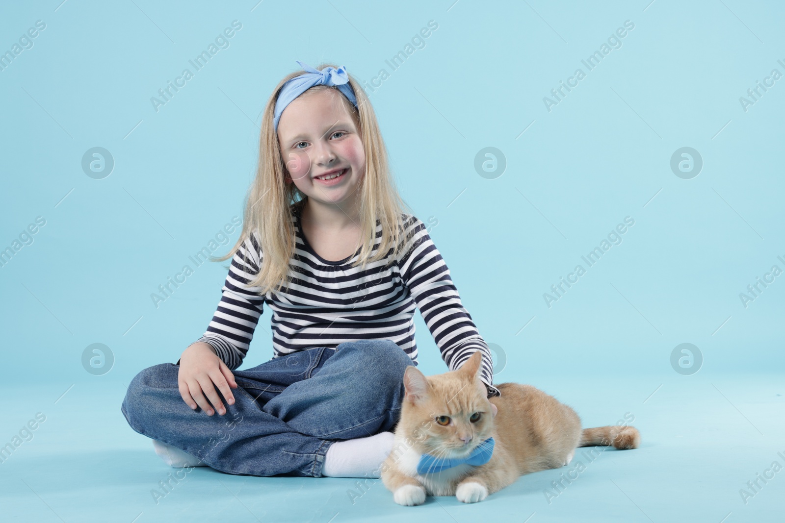 Little girl with her cute ginger cat on light blue background Photo of Little girl with her cute ginger cat on light blue background