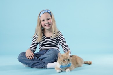 Photo of Little girl with her cute ginger cat on light blue background
