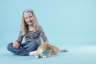 Photo of Little girl with her cute ginger cat on light blue background, space for text