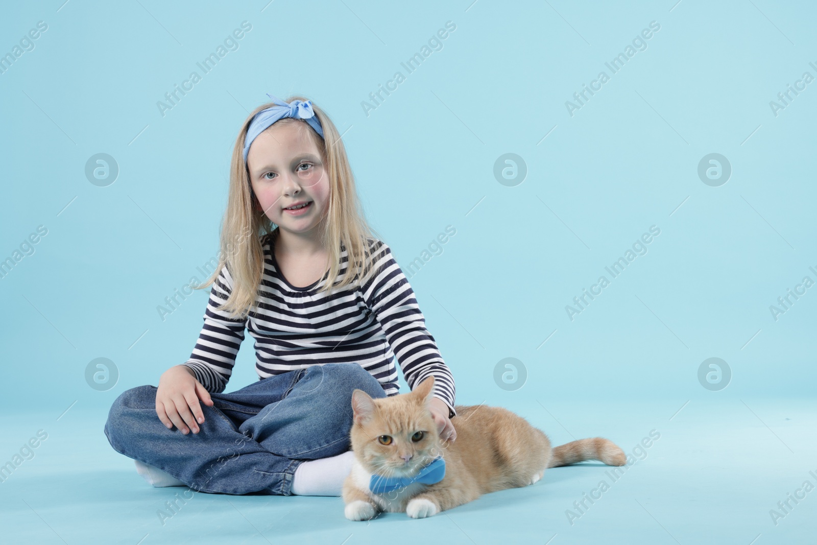 Little girl with her cute ginger cat on light blue background, space for text Photo of Little girl with her cute ginger cat on light blue background, space for text