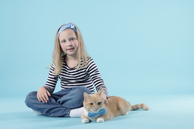 Photo of Little girl with her cute ginger cat on light blue background, space for text