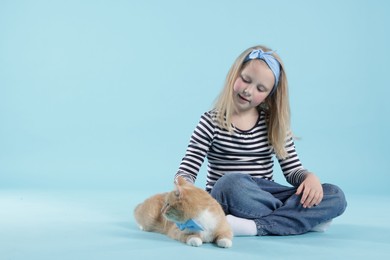 Photo of Little girl with her cute ginger cat on light blue background, space for text