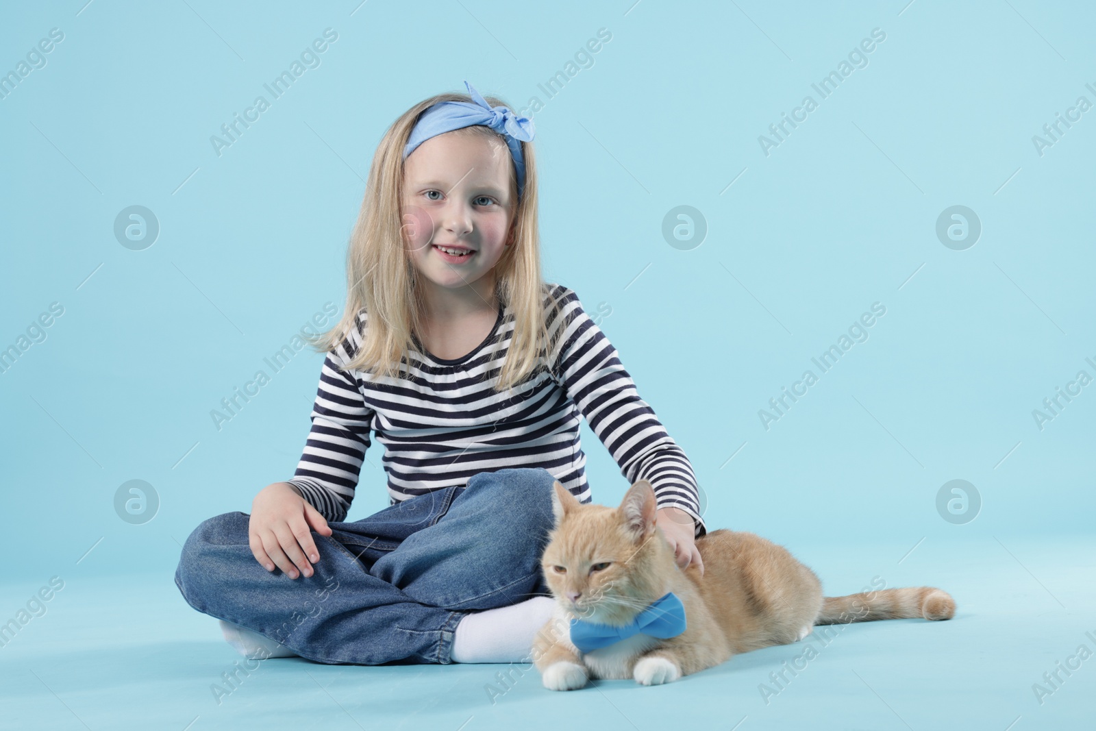 Little girl with her cute ginger cat on light blue background Photo of Little girl with her cute ginger cat on light blue background