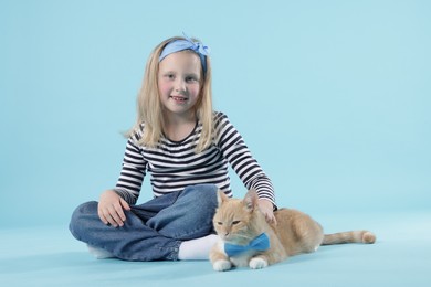Photo of Little girl with her cute ginger cat on light blue background