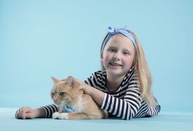 Photo of Little girl with her cute ginger cat on light blue background