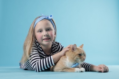 Photo of Little girl with her cute ginger cat on light blue background