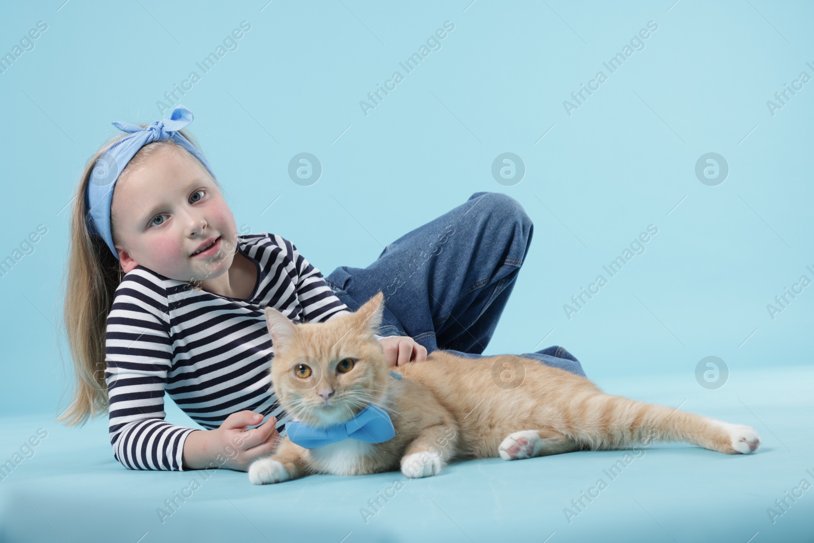 Little girl with her cute ginger cat on light blue background Photo of Little girl with her cute ginger cat on light blue background