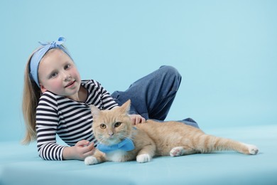 Photo of Little girl with her cute ginger cat on light blue background