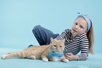 Photo of Little girl with her cute ginger cat on light blue background