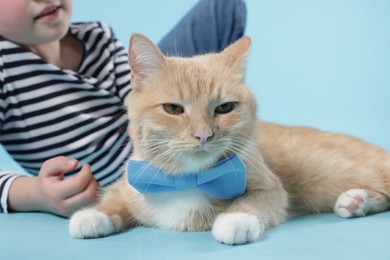 Photo of Little girl with her cute ginger cat on light blue background, closeup