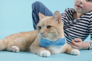 Photo of Little girl with her cute ginger cat on light blue background, closeup