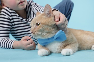 Photo of Little girl with her cute ginger cat on light blue background, closeup