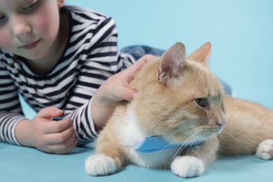 Photo of Little girl with her cute ginger cat on light blue background, selective focus
