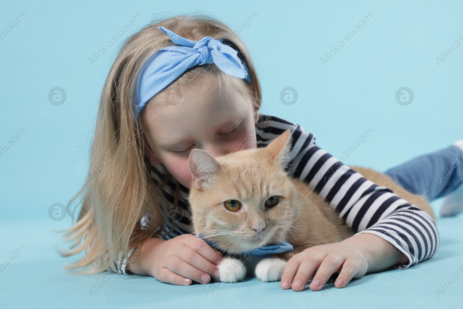 Little girl with her cute ginger cat on light blue background Photo of Little girl with her cute ginger cat on light blue background