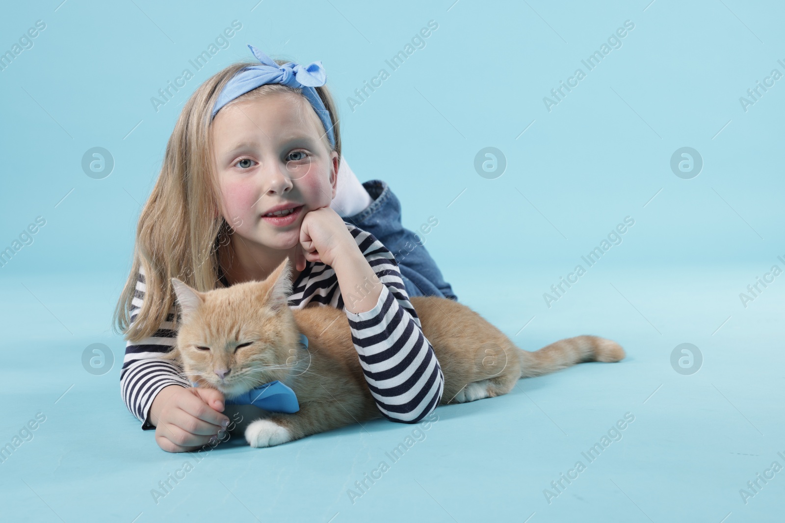 Little girl with her cute ginger cat on light blue background, space for text Photo of Little girl with her cute ginger cat on light blue background, space for text