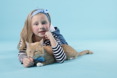 Photo of Little girl with her cute ginger cat on light blue background, space for text