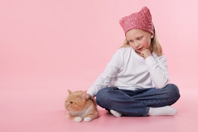 Photo of Little girl with her cute ginger cat on pink background, space for text
