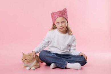 Photo of Little girl with her cute ginger cat on pink background