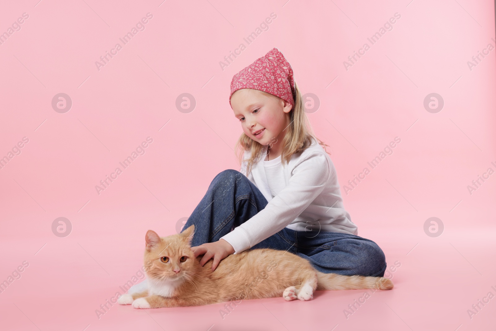 Little girl with her cute ginger cat on pink background Photo of Little girl with her cute ginger cat on pink background