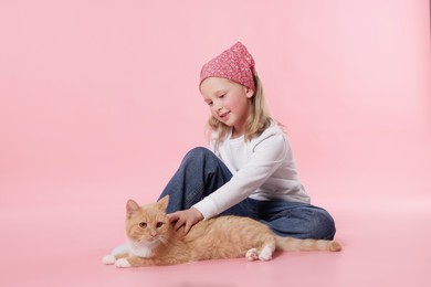 Photo of Little girl with her cute ginger cat on pink background