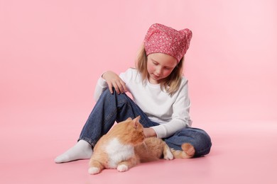 Photo of Little girl with her cute ginger cat on pink background