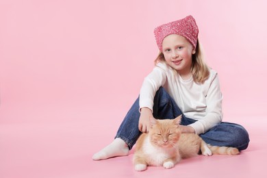 Photo of Little girl with her cute ginger cat on pink background, space for text