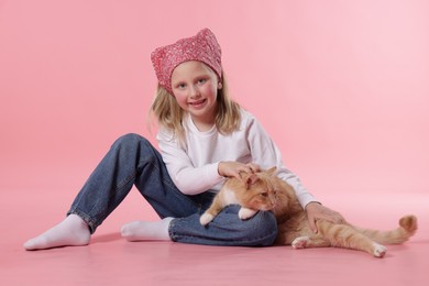 Photo of Little girl with her cute ginger cat on pink background