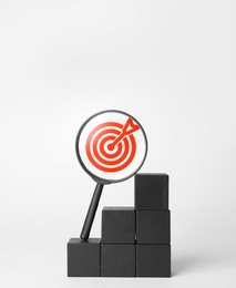 Image of Targeting. Magnifying glass with bullseye inside and stacked cubes on light background