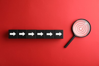 Image of Targeting. Cubes with arrows pointing at magnifying glass with bullseye inside on red background, top view