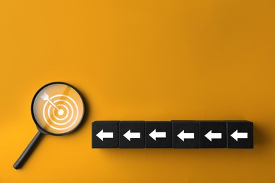 Image of Targeting. Cubes with arrows pointing at magnifying glass with bullseye inside on orange background, top view