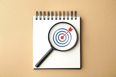 Image of Targeting. Notebook with bullseye and magnifying glass on dark beige background, top view