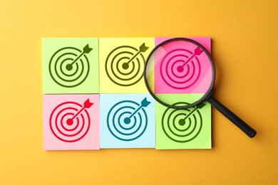 Image of Targeting. Paper notes with bullseye and magnifying glass on orange background, top view