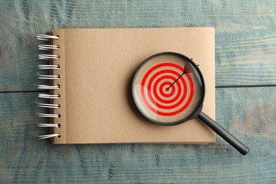 Image of Targeting. Notebook with bullseye and magnifying glass on wooden background, top view
