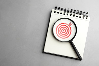 Image of Targeting. Notebook with bullseye and magnifying glass on grey background, top view. Space for text