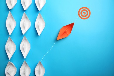 Image of Targeting. Orange paper boat among white ones heading to bullseye on light blue background, top view