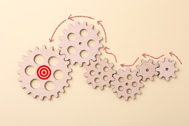 Image of Targeting. Wooden cogwheels and one with bullseye on beige background, top view. Arrows showing direction of movement