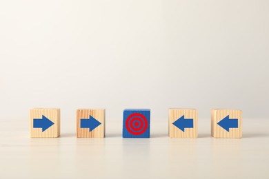Image of Targeting. Wooden cubes with arrows pointing at blue one with bullseye on table