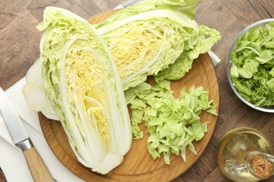 Photo of Fresh cut Chinese cabbage, oil and knife on wooden table, flat lay