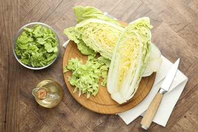 Photo of Fresh cut Chinese cabbage, oil and knife on wooden table, flat lay