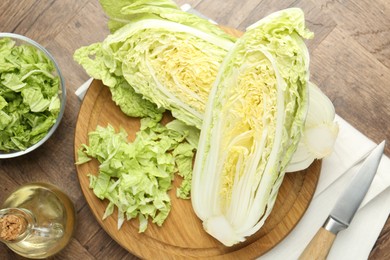 Photo of Fresh cut Chinese cabbage, oil and knife on wooden table, flat lay