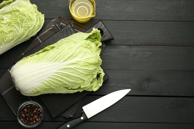 Photo of Fresh Chinese cabbages, oil, knife and peppercorns on black wooden table, flat lay. Space for text