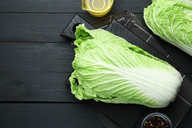 Photo of Fresh Chinese cabbages, oil and peppercorns on black wooden table, flat lay. Space for text
