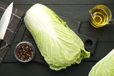Photo of Fresh Chinese cabbages, oil, knife and peppercorns on black wooden table, flat lay