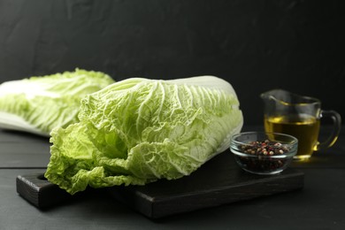 Photo of Fresh Chinese cabbages, oil and peppercorns on black wooden table, closeup