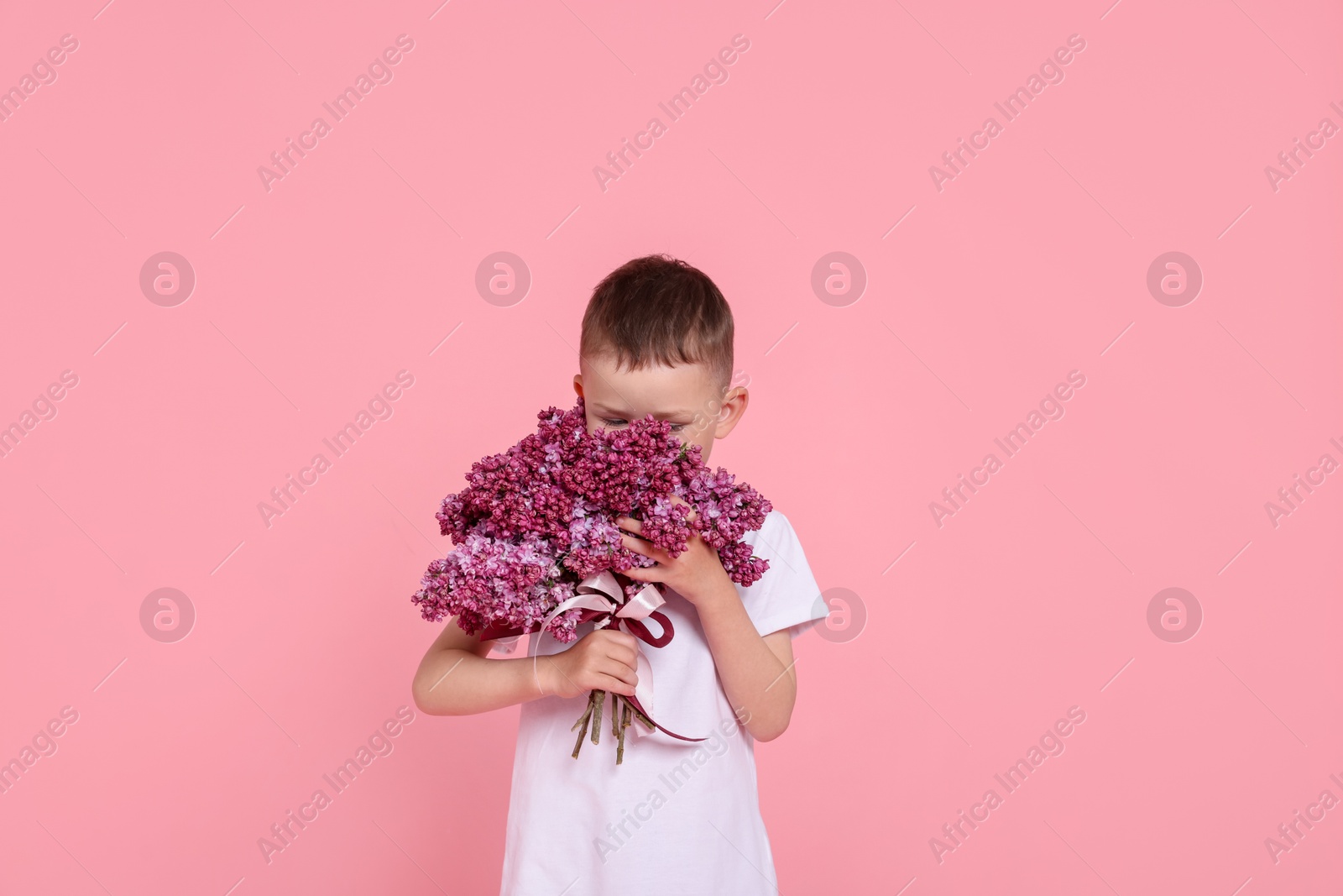 Little boy with bouquet of lilac flowers on pink background Photo of Little boy with bouquet of lilac flowers on pink background
