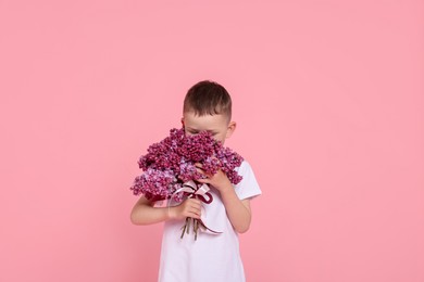Photo of Little boy with bouquet of lilac flowers on pink background