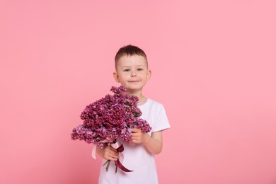 Photo of Little boy with bouquet of lilac flowers on pink background