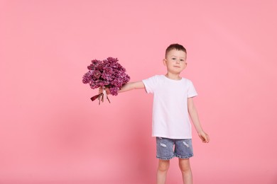 Photo of Little boy with bouquet of lilac flowers on pink background