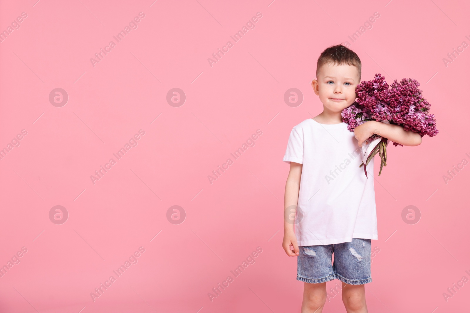 Little boy with bouquet of lilac flowers on pink background, space for text Photo of Little boy with bouquet of lilac flowers on pink background, space for text